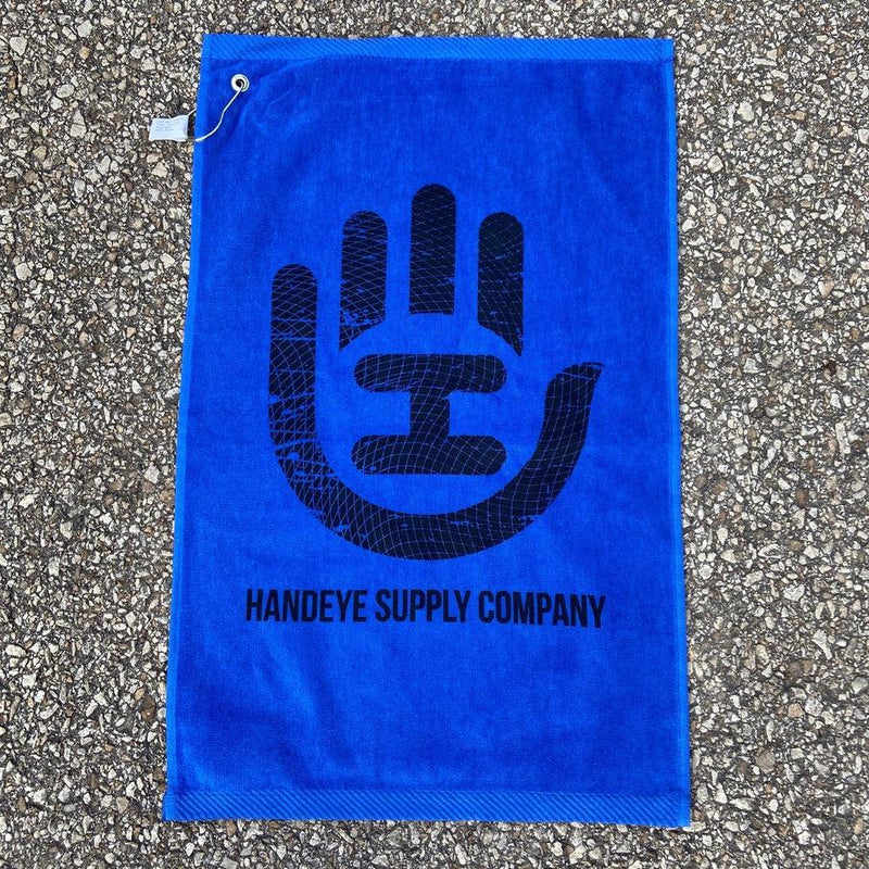 Bright blue Handeye Supply Company disc golf towel featuring a large black hand logo and a hanging loop.