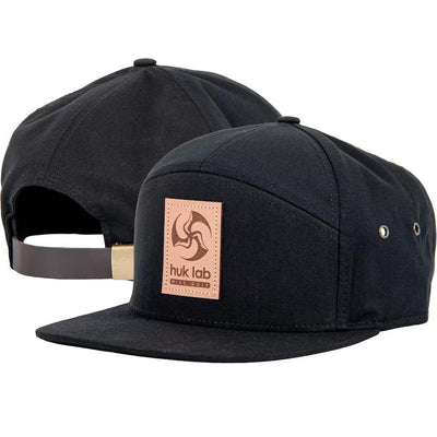 Two black Huk Lab Trifly hats feature a light brown leather patch with a darker brown swirl logo and text.