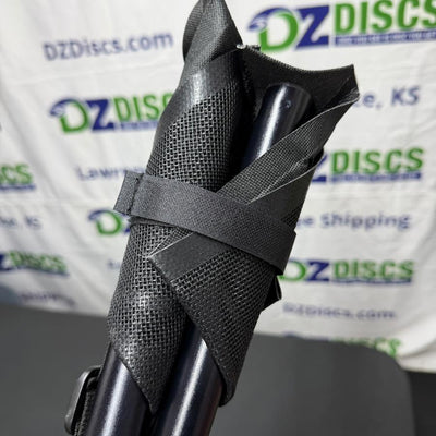 Folded Huk Lab tripod stool with black metal legs and mesh fabric, secured by a woven strap.