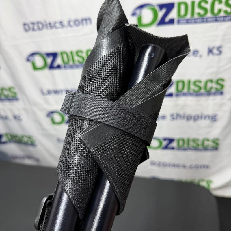 Folded Huk Lab tripod stool with black metal legs and mesh fabric, secured by a woven strap.