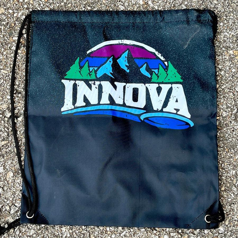 Black Innova drawstring bag with a colorful mountain and forest logo, including a blue disc golf putter.
