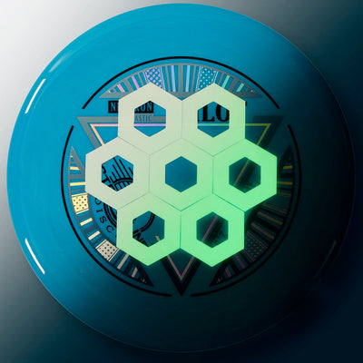 Blue Innova disc golf disc with a reflective, iridescent foil stamp and a glow-in-the-dark hexagonal overlay.