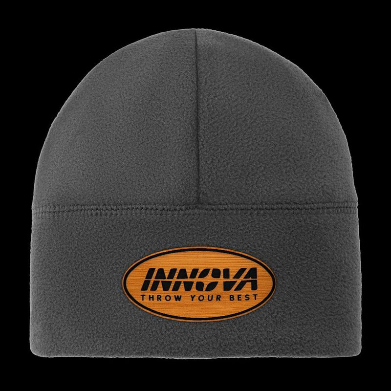 Dark gray fleece Innova beanie featuring an oval, woodgrain Inova "Throw Your Best" patch with black text.