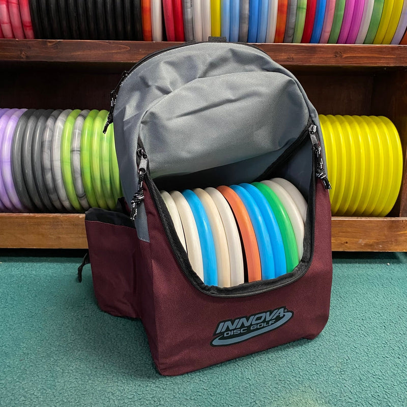 Maroon Innova Discover disc golf bag with a gray top compartment filled with multiple colorful discs.