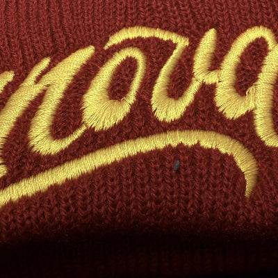 Close-up of a red Innova Flow cuff beanie, featuring "Flow" embroidered in stylized yellow script lettering.