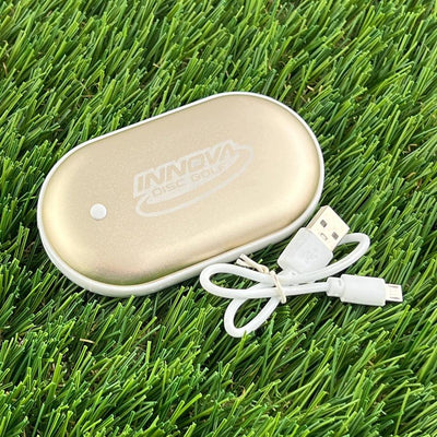 Gold Innova "Disc Golf" rechargeable hand warmer with a textured top and a white charging cord.