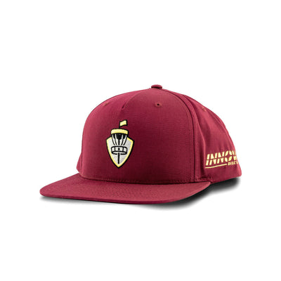Maroon Innova flatbill snapback hat with a yellow embroidered disc golf basket shield logo and bold yellow Innova lettering.