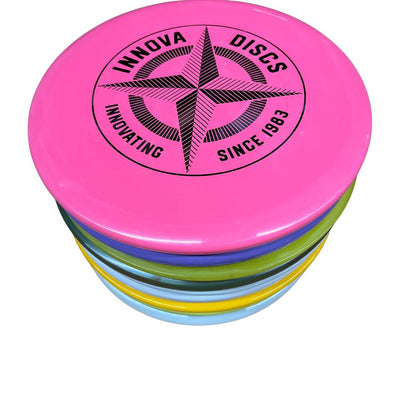 A colorful stack of assorted Innova disc golf discs with the top disc in bright pink featuring a black compass logo.