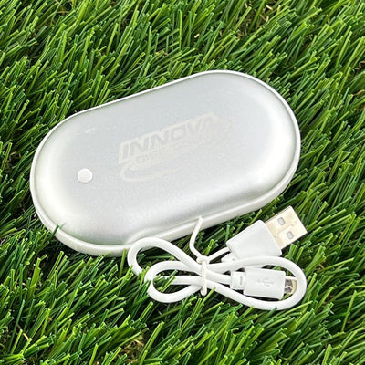 Silver metallic Innova rechargeable hand warmer with a small white indicator light and a coiled white USB charging cable.