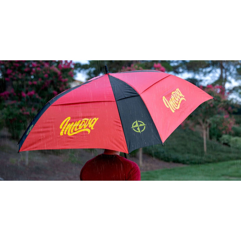 Red and black Innova Flow umbrella with a yellow Innova logo and a green compass rose design protecting a person from rain.