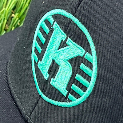 Black flexfit Kastaplast clothback hat with an embroidered bright teal "K" logo inside an outline.