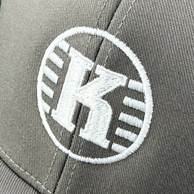 Flexfit Kastaplast clothback hat featuring a white embroidered 'K' logo in a circular design on gray fabric.