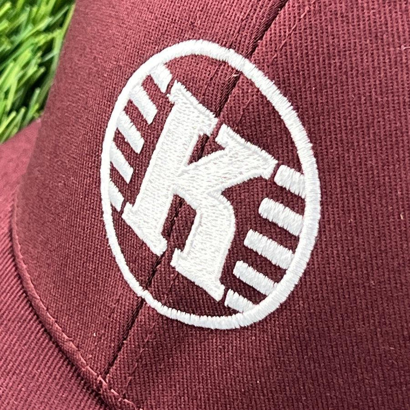 Maroon Flexfit Kastaplast disc golf hat with a white embroidered "K" logo and circular design on the front.
