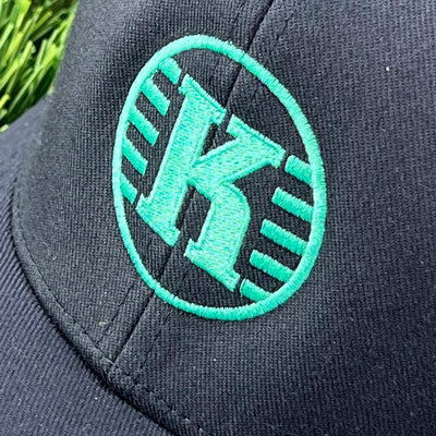 Close-up of a navy blue Kastaplast Flexfit hat featuring a bright green embroidered Kastaplast logo.
