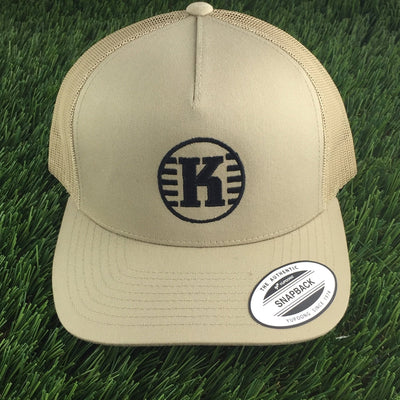 Tan Yupoong Kastaplast snapback meshback hat features a black "K" logo in a circle on the front.