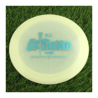 Translucent white Latitude 64 Opto X Stiletto disc golf driver with a blue 10 Year Anniversary sword stamp.