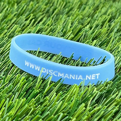 Light blue discmania "reinvent" wristband with "www.discmania.net" text, resting on artificial green grass.