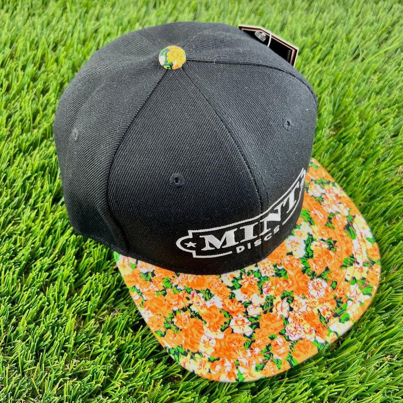 Black Mint Discs flat bill snapback hat with white Mint Discs logo and an orange floral pattern on the visor.