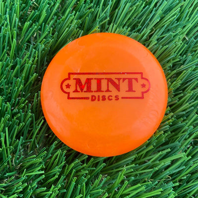 Bright orange Mint Discs Zing Pico mini disc golf marker with a red foil Mint Discs logo stamp.