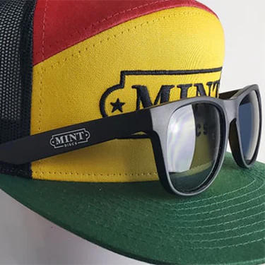 Mint Sunglasses black wayfarer style sunglasses with the MINT logo on the temple sit on a colorful cap.
