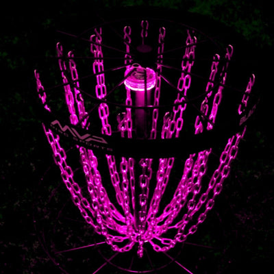 Mvp black lunar module disc golf basket with neon pink illuminated chains and a bright pink inner light glowing in the dark.