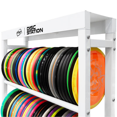 White MVP Disc Station storage rack with multiple shelves holding colorful discs, including an orange one.