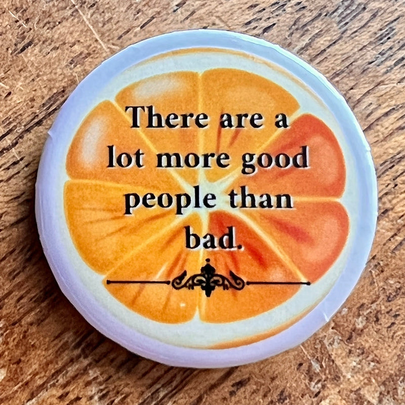 Round novelty button with an orange slice design and the text "There are a lot more good people than bad.".