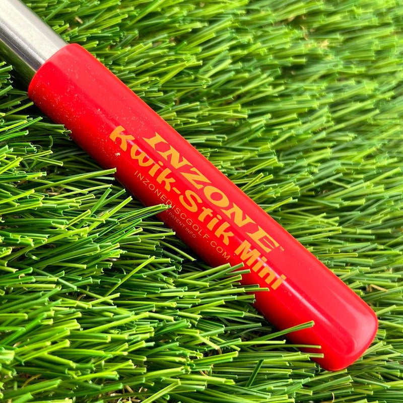 A red plastic inzone kwik-stik mini disc golf retriever with yellow text, resting on green artificial turf.
