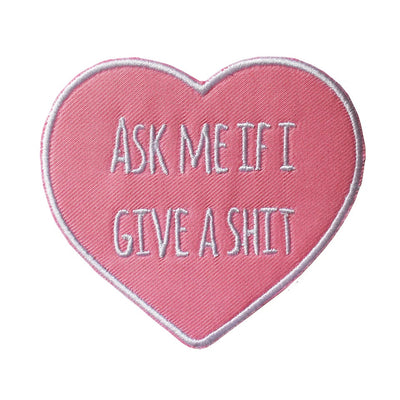 Pink heart-shaped embroidered patch with "ASK ME IF I GIVE A SHIT" text in white stitching and a white border.