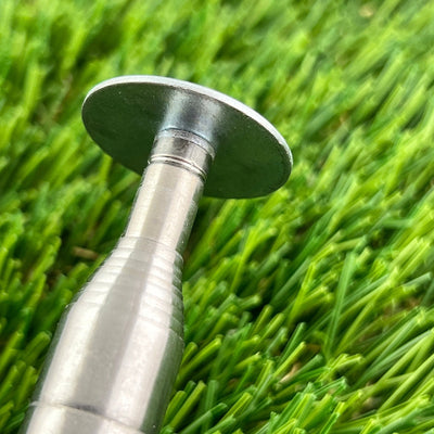 A shiny silver "inzone kwik stik mini round hook" with a flat, circular top, partially visible on green synthetic turf.