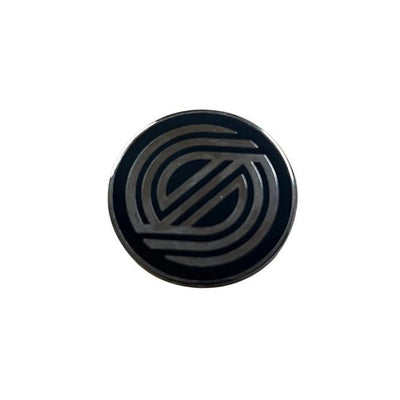 Circular black metal enamel pin with a silver concentric line design that forms an S shape in the center.