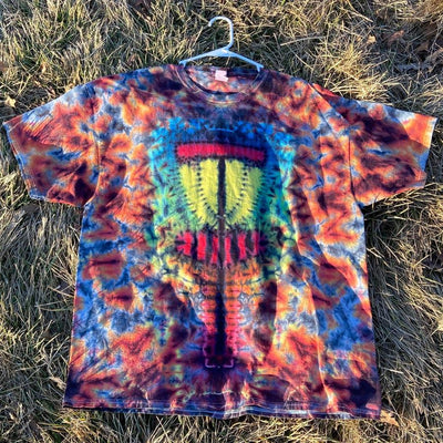 A vibrant tie-dye Twisted Amanita basket-style t-shirt with a detailed yellow, red, and blue disc golf basket graphic.
