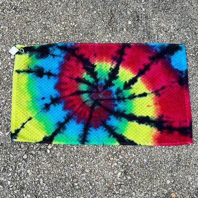 Rectangular tie-dye towel with a vibrant black, red, yellow, and blue swirl pattern, featuring a white clip.