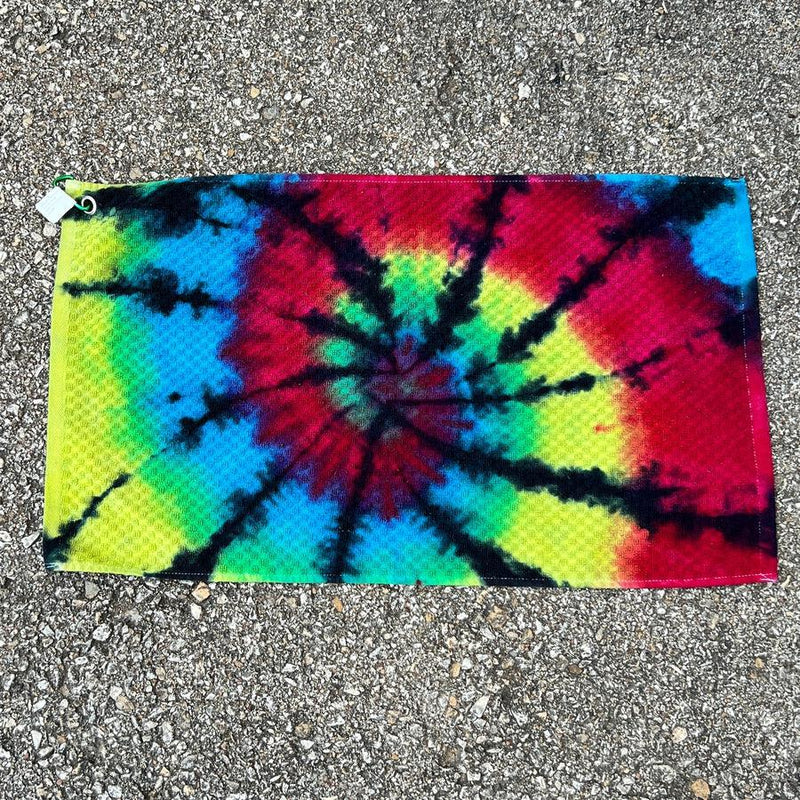 Rectangular tie-dye towel with a vibrant black, red, yellow, and blue swirl pattern, featuring a white clip.