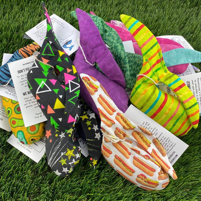 A pile of colorful Whale Sac grip bags, one featuring a pattern of hotdogs on white fabric.