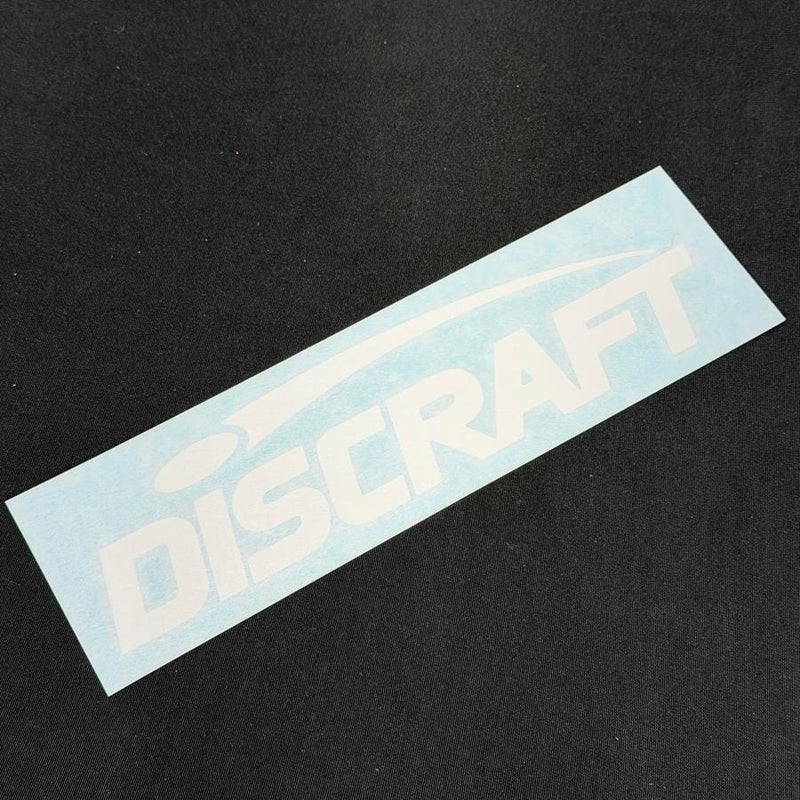 White "discraft" decal with a faint blue protective layer, angled diagonally on a dark textured background.