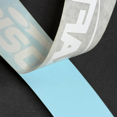 A white discraft decal with partially peeled transparent transfer tape, revealing the light blue backing paper against a.