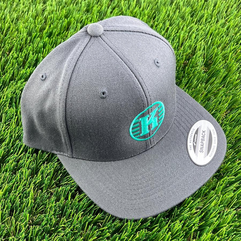 Gray Yupoong Kastaplast Snapback hat with a vibrant teal K logo and visible authenticity sticker.