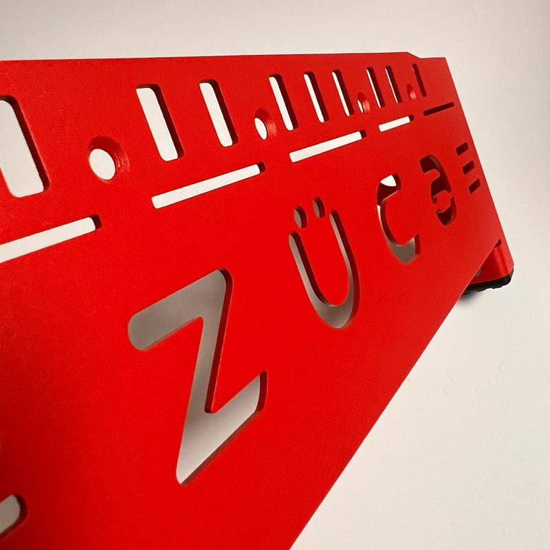 Textured red metal ZÜCA front wrapper for a backpack cart, featuring stylized cut-out letters and slots.